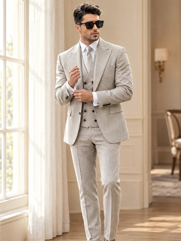Groom in a light grey three-piece slim fit suit with silver tie adjusting his cufflinks by a tall window
